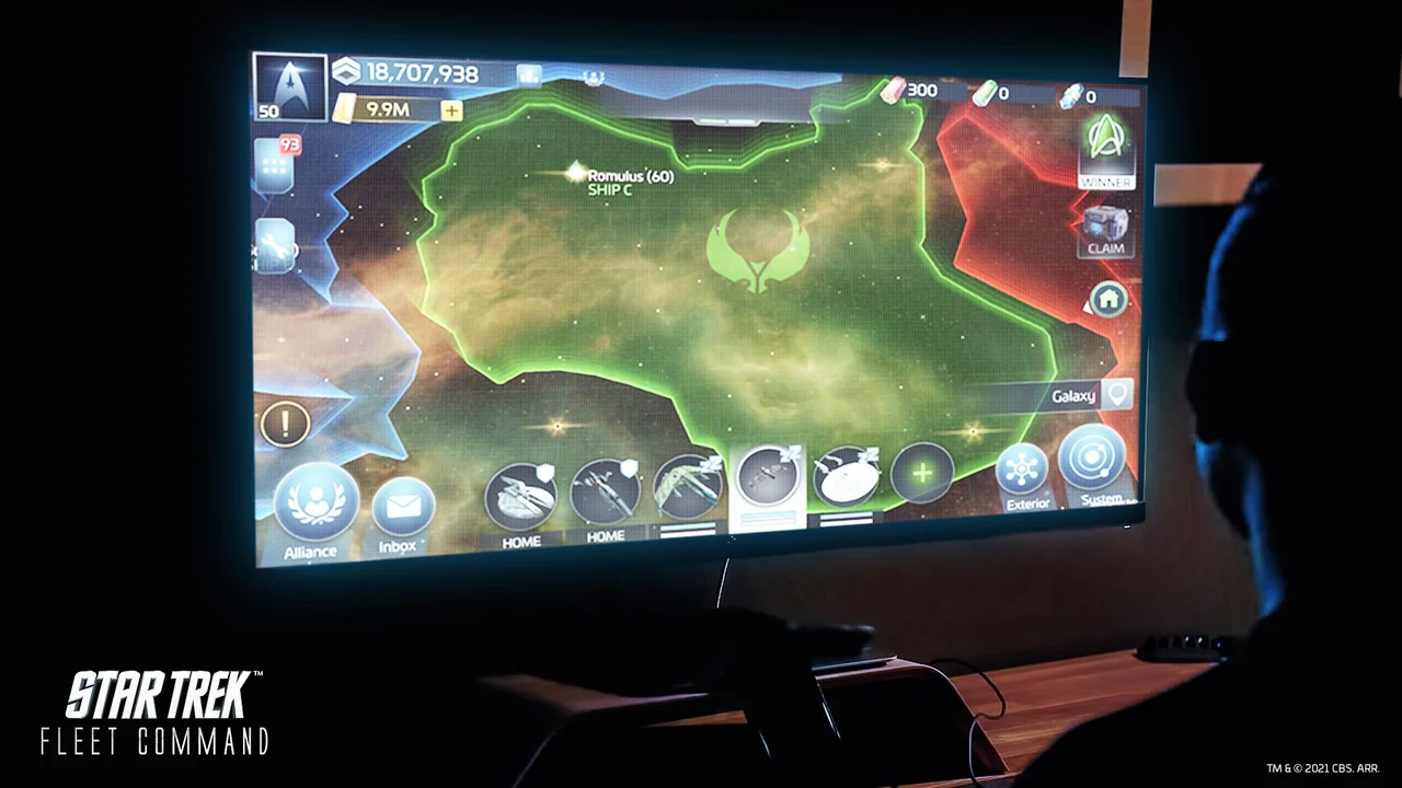 A player in a dark room faces a desktop monitor showing the game's galaxy map around Romulan territory.